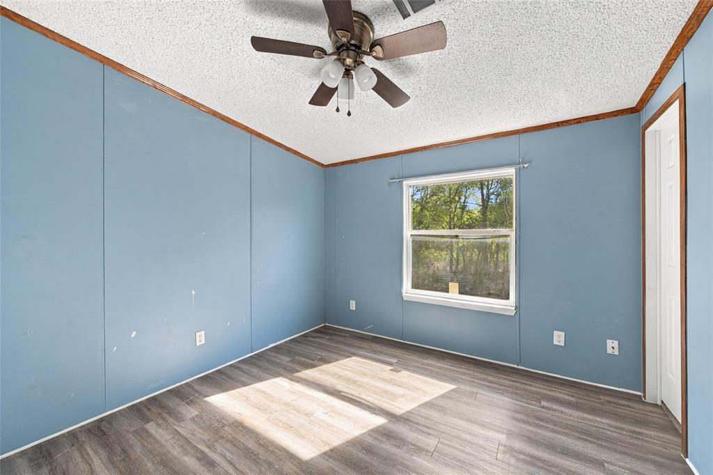 Wood-finish flooring, ceiling fan with integrated light fixture, single-pane window, and wood-trim crown molding