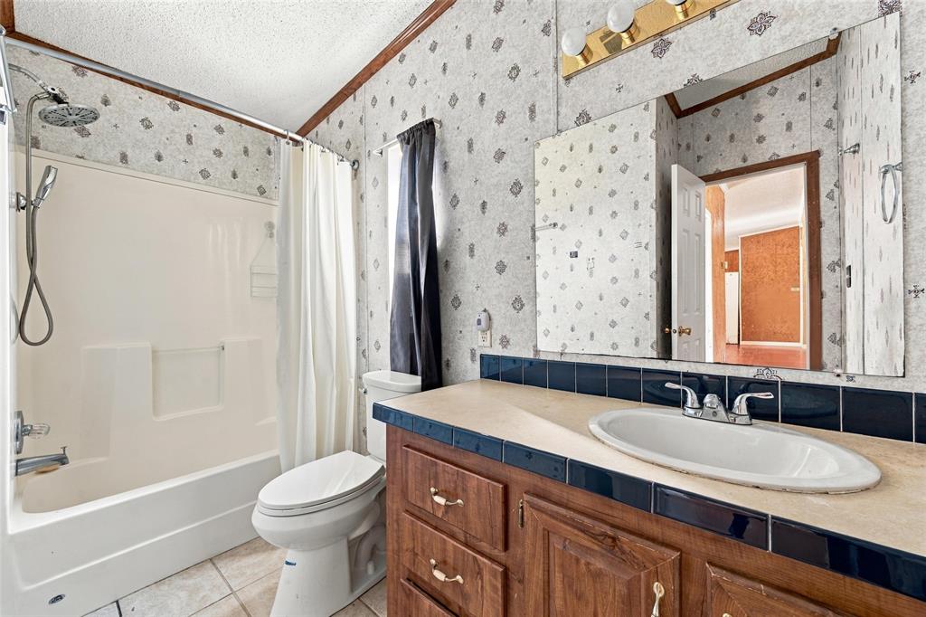 Bathroom featuring a tub-shower combination with a surround, wood-finish vanity cabinetry, a solid-surface countertop with an integrated basin, and a wall-mounted mirror with integrated lighting