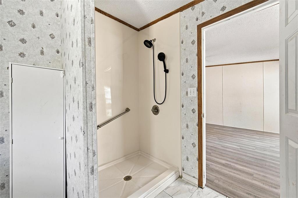 Walk-in shower enclosure featuring smooth-surface surround panels, a handheld showerhead, a metal grab bar, and wood-finish flooring in the room beyond