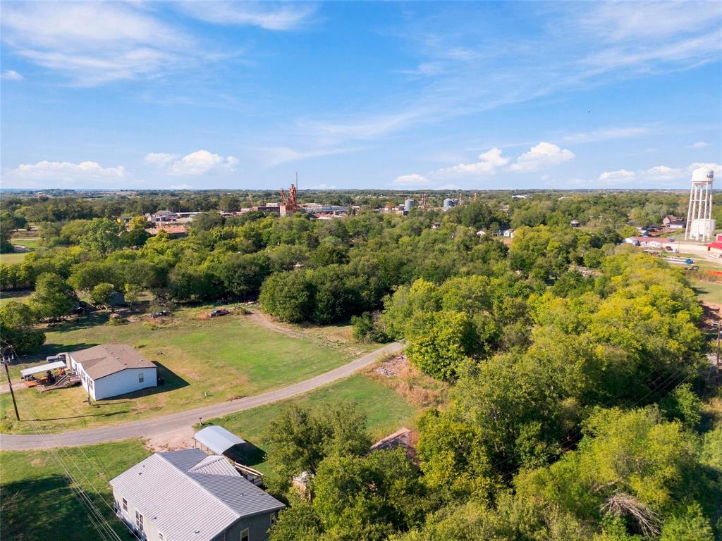 Aerial perspective featuring expansive acreage, mature tree clusters, open grass fields, and established road access