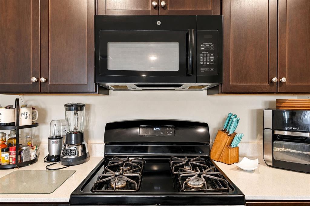 Dark-finish cabinetry paired with a black gas range and integrated over-the-range microwave, complemented by neutral-toned countertops