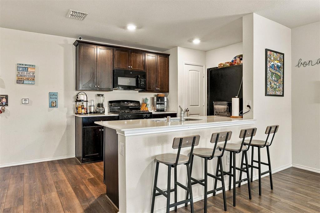 Kitchen featuring dark wood cabinetry, a light-toned stone-surface peninsula, wood-finish flooring, and built-in black appliances
