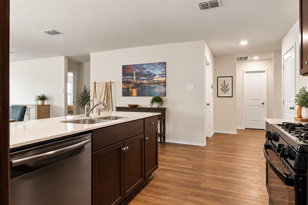 Kitchen featuring a stone-surface countertop, dark wood cabinetry, stainless steel dishwasher, gas range, and wood-finish flooring