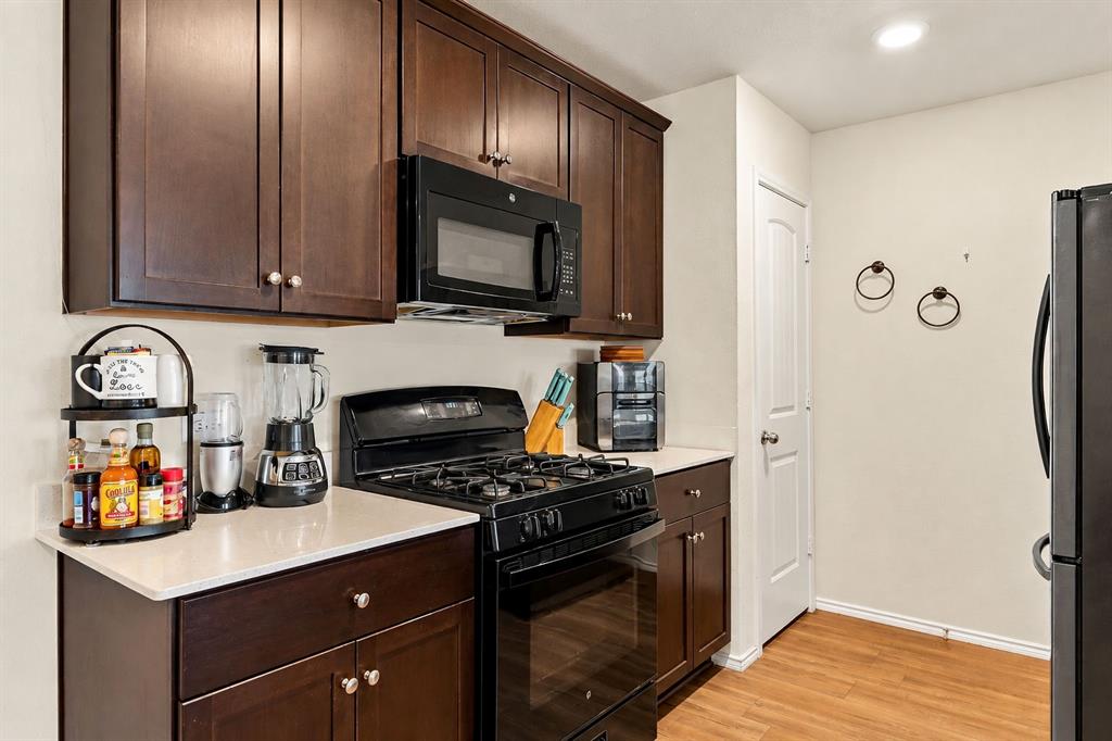 Kitchen featuring dark wood cabinetry, solid-surface countertops, built-in gas range with overhead microwave, and wood-finish flooring