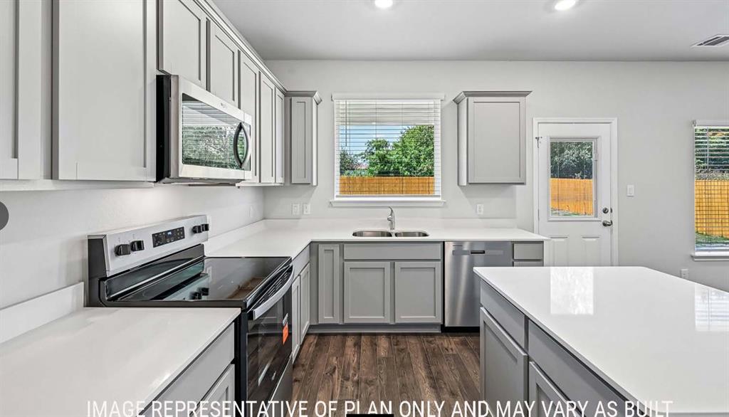 Kitchen featuring light-toned cabinetry, solid surface countertops, a central island, stainless steel appliances, and wood-finish flooring Kitchen featuring light-toned cabinetry, solid surface countertops, a central island, stainless steel appliances, and wood-finish flooring