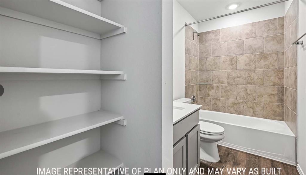Built-in shelving, vanity with stone-style countertop, tub-shower combination with tile surround, and wood-finish flooring