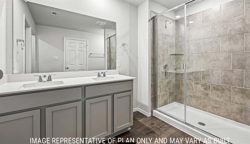 Dual-sink vanity with neutral cabinetry, large wall-to-wall mirror, walk-in shower with tile surround, glass enclosure, and wood-finish flooring