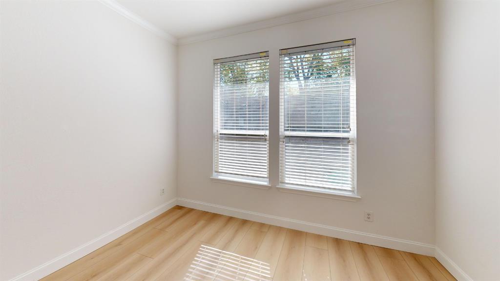 Neutral-toned interior space featuring light wood-finish flooring, crown molding, and dual windows equipped with horizontal blinds