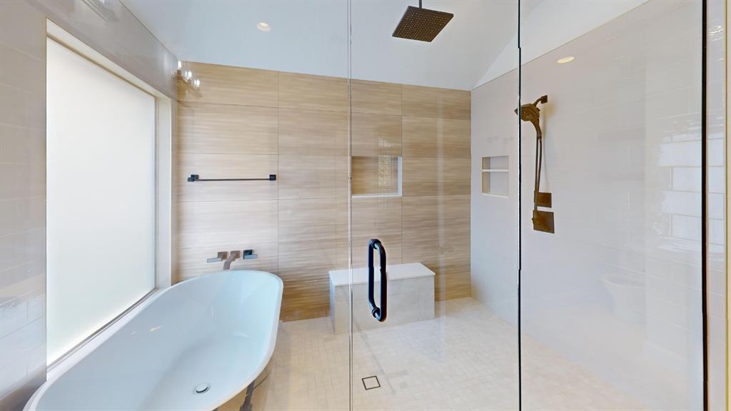Freestanding soaking tub with wall-mounted fixtures, frameless glass shower enclosure, wood-finish tile wall surround, built-in tiled shower bench, and recessed wall niche