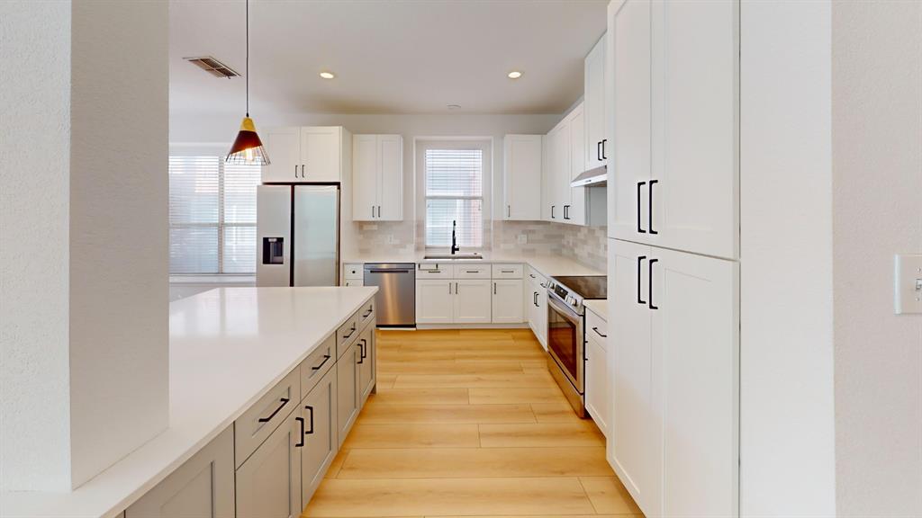Kitchen featuring white shaker-style cabinetry, a quartz-topped central island, stainless steel appliances, light-toned wood-finish flooring, and recessed lighting