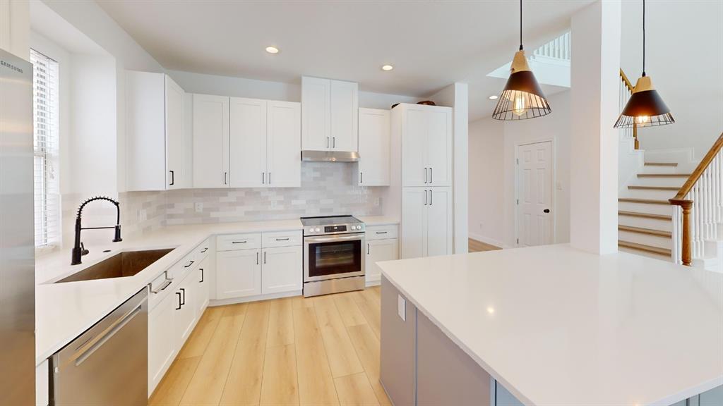 Kitchen featuring white shaker-style cabinetry, solid-surface countertops, subway tile backsplash, stainless steel appliances, and wood-finish flooring