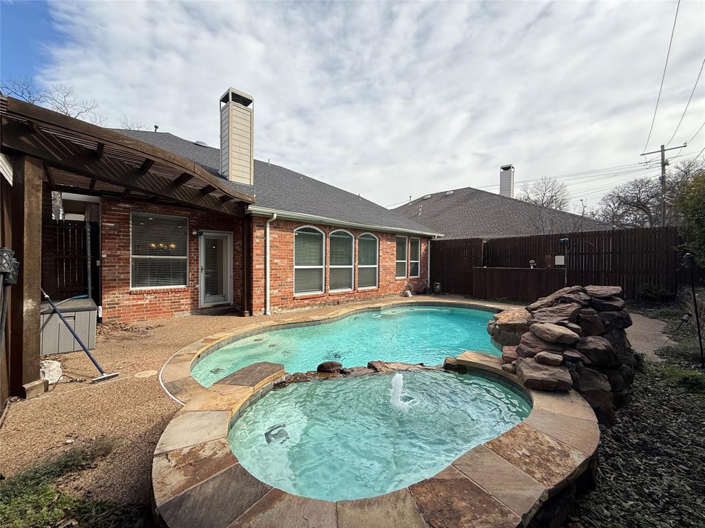 Brick exterior featuring a swimming pool, attached spa with water feature, stone rock formation, and covered patio area