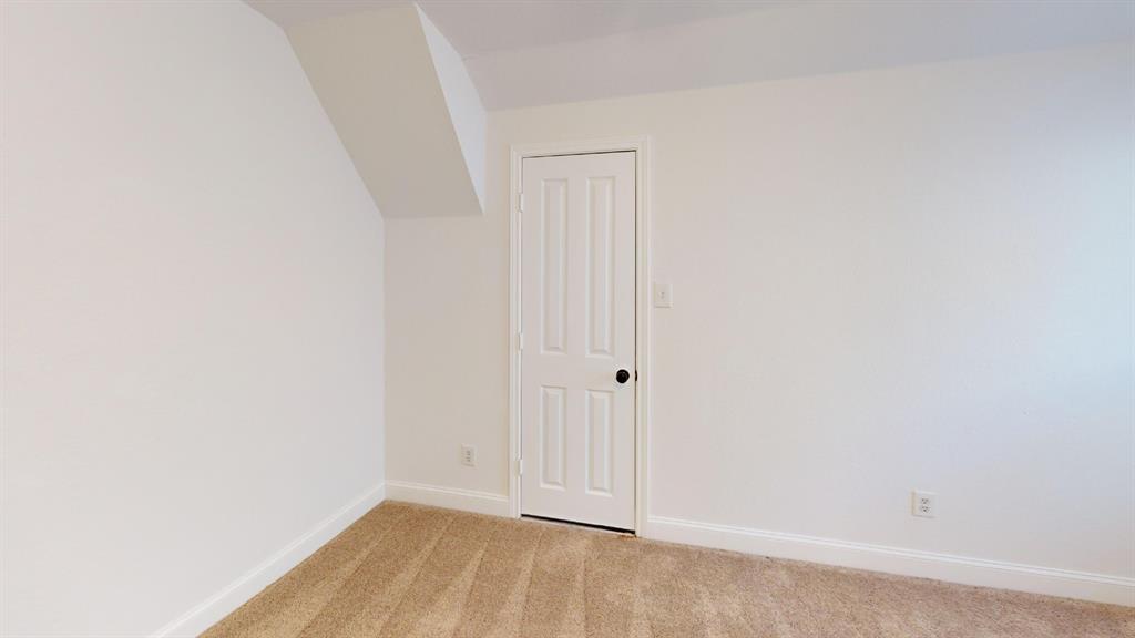Neutral-toned carpeted flooring, white interior walls, and a four-panel interior door with matte black hardware