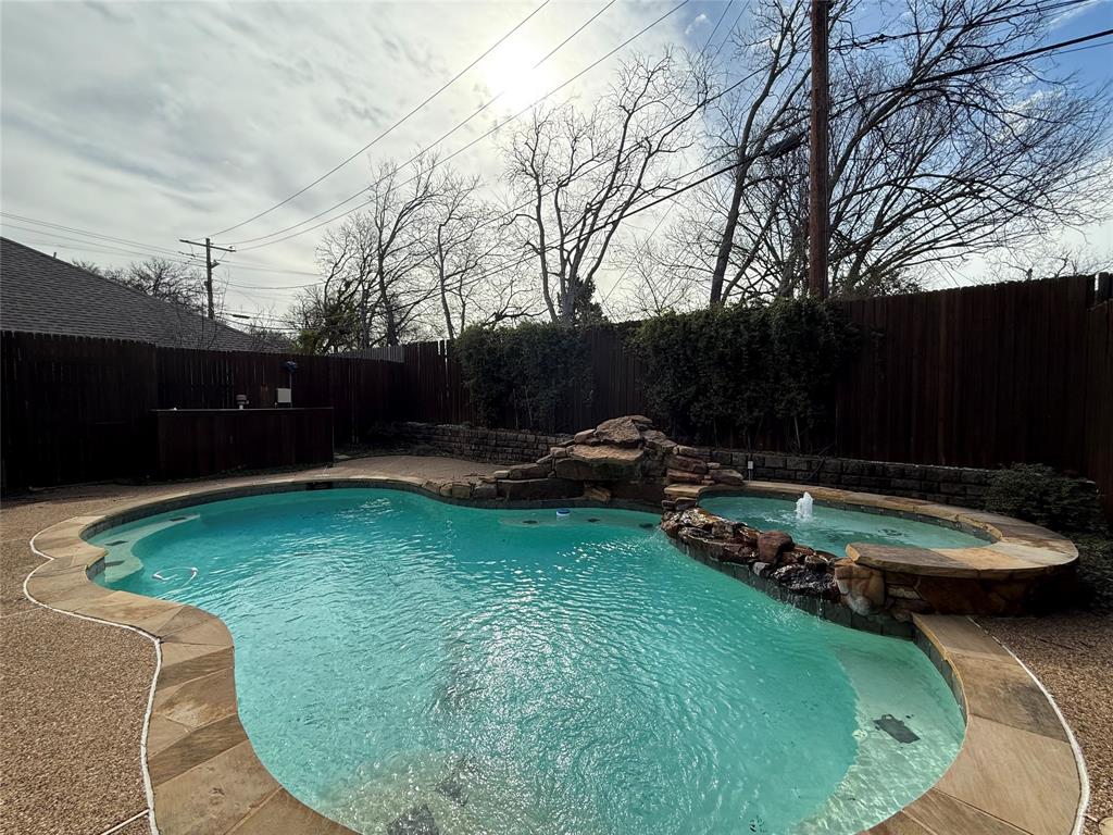 Freeform swimming pool with a stone rock feature, integrated spa, built-in water fountain, and surrounding stone coping