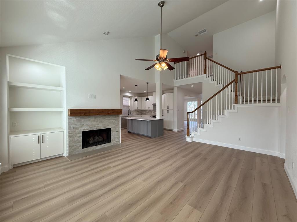 Vaulted ceilings, wood-finish flooring, built-in cabinetry, stone-surround fireplace with a wooden mantel, and staircase with white railings