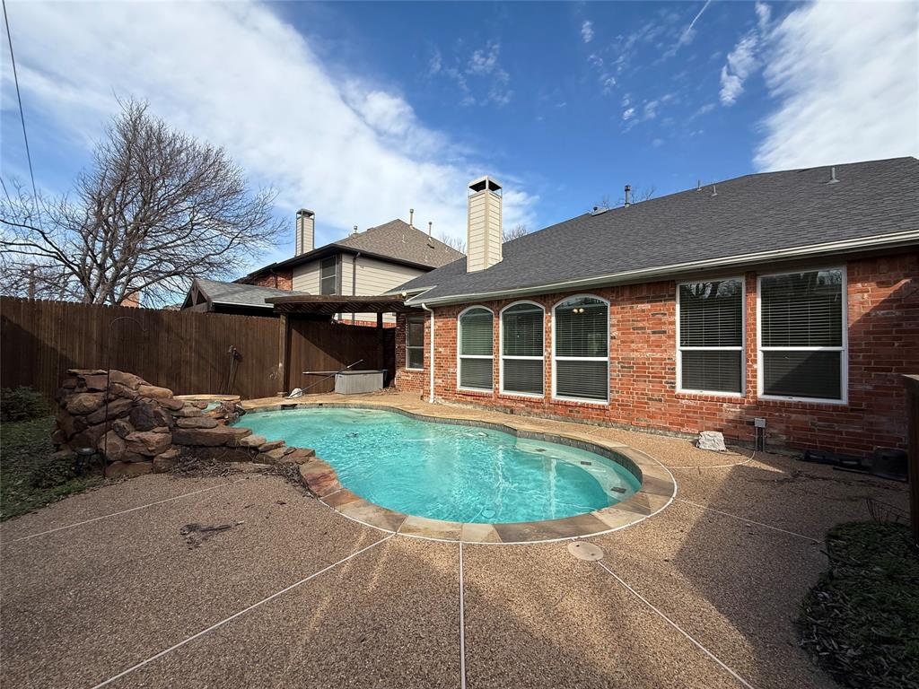 Backyard featuring an in-ground swimming pool, stone water feature, aggregate concrete decking, and wood privacy fencing