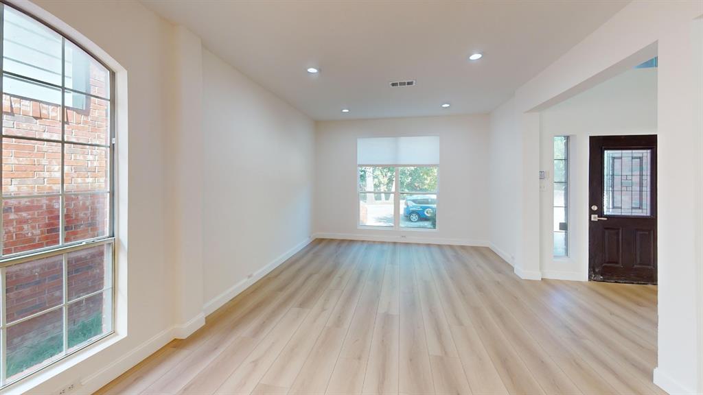 Open interior space featuring light-tone wood-finish flooring, recessed lighting, expansive windows, and a dark-finish front door with decorative glass paneling