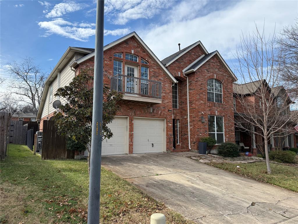 Multi-story brick exterior featuring a balcony with metal railing, arched window accents, and a two-car garage