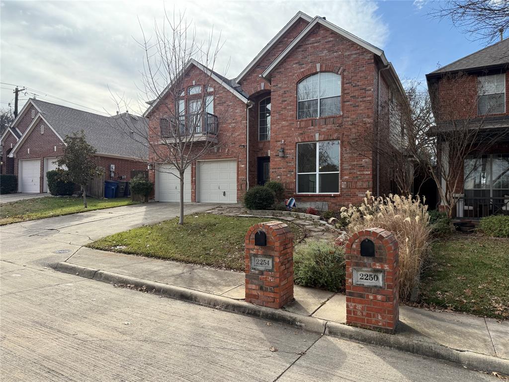 Two-story brick exterior featuring a multi-gabled roofline, an integrated two-car garage, an upper-level balcony, and matching brick mailbox pillars