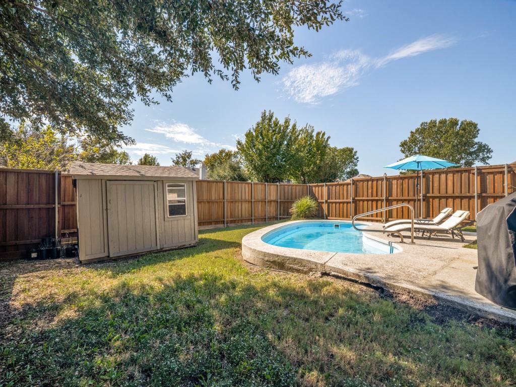 Backyard featuring an inground pool with concrete decking, a wooden perimeter fence, and a storage shed