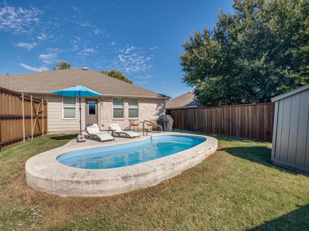 Oval-shaped swimming pool with concrete decking, enclosed by a full-height wood privacy fence and featuring an exterior storage shed