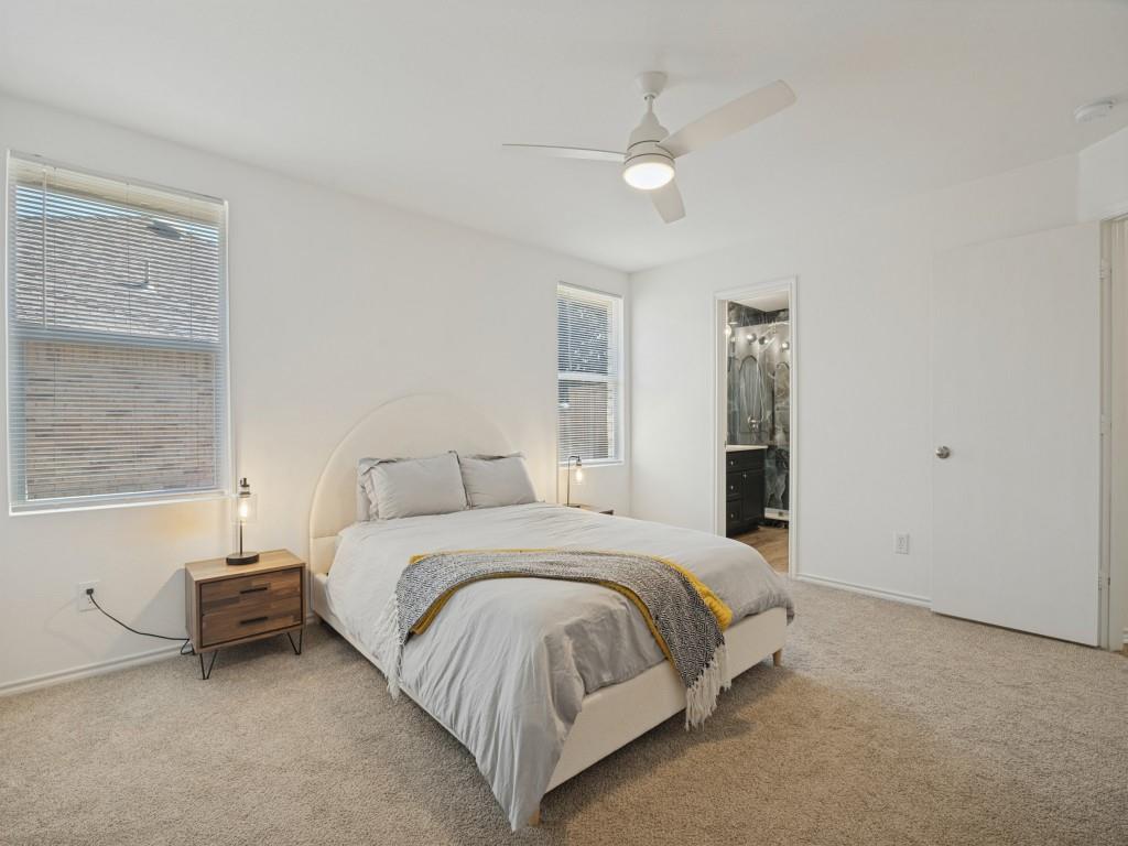 Neutral-toned carpeting, white walls, dual windows with blinds, and a white ceiling fan with integrated lighting