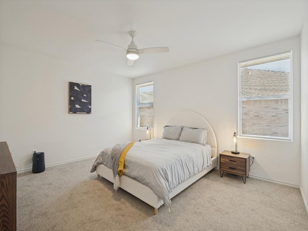 Neutral-toned carpeted flooring, dual windows with integrated blinds, and a white ceiling fan with an attached light fixture