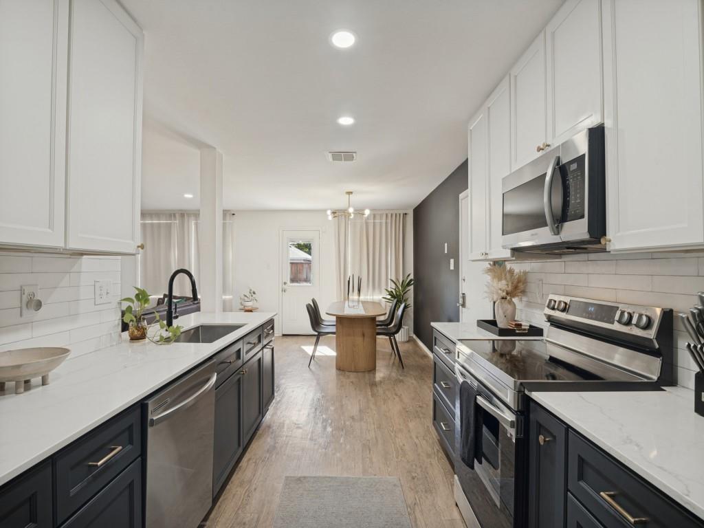 Kitchen featuring two-tone shaker cabinetry, light-toned stone countertops, white subway tile backsplash, stainless steel appliances, and wood-finish flooring