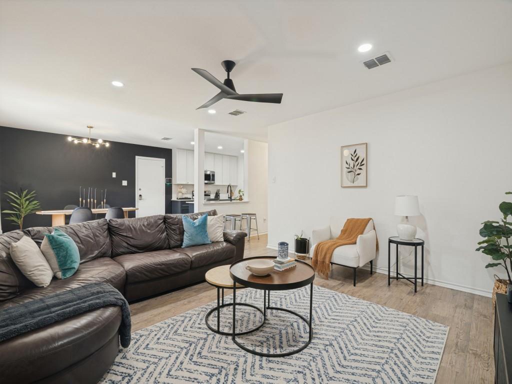 Open-concept interior featuring wood-finish flooring, a matte black three-blade ceiling fan, recessed lighting, and a contrasting charcoal-colored accent wall