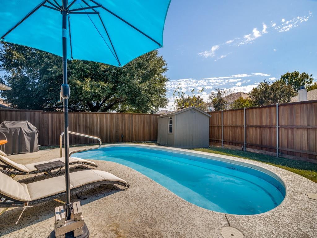 Backyard featuring an inground pool with a textured concrete deck, enclosed by a wood privacy fence and including a storage shed