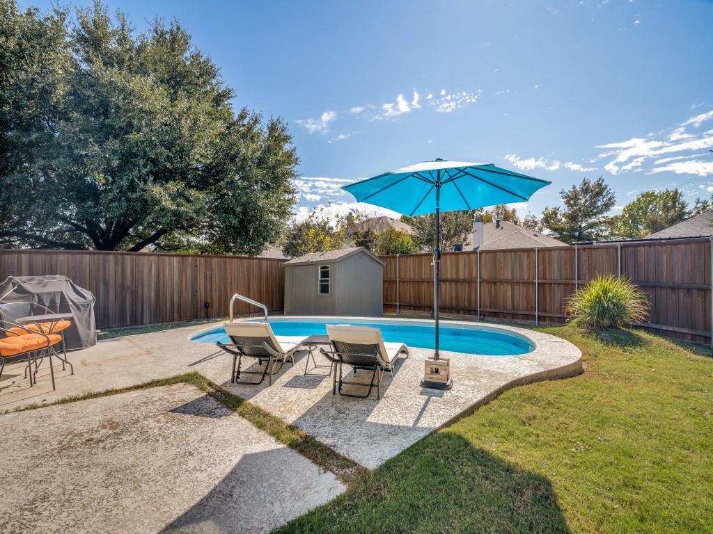 Backyard featuring an in-ground swimming pool, concrete decking, wood privacy fencing, and a detached storage structure