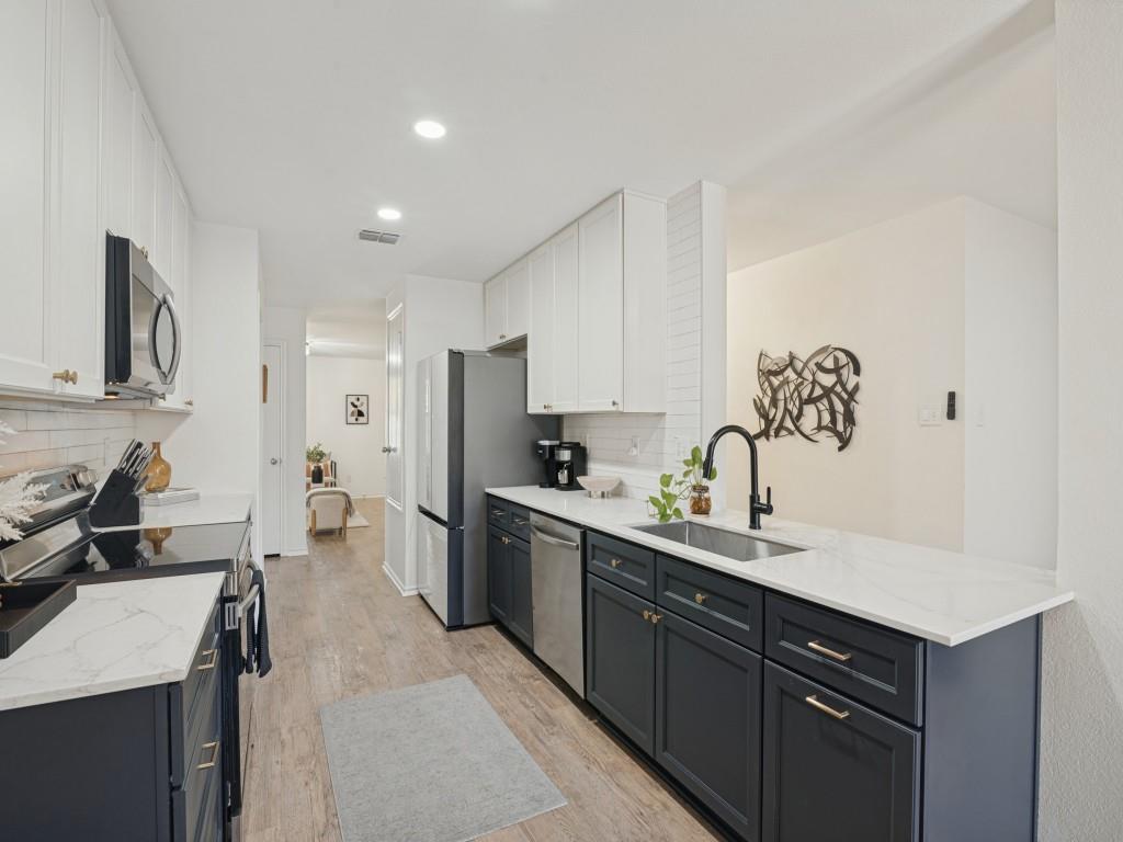 Kitchen featuring dual-tone cabinetry, stone-finish countertops, stainless steel appliances, a white tile backsplash, and wood-finish flooring