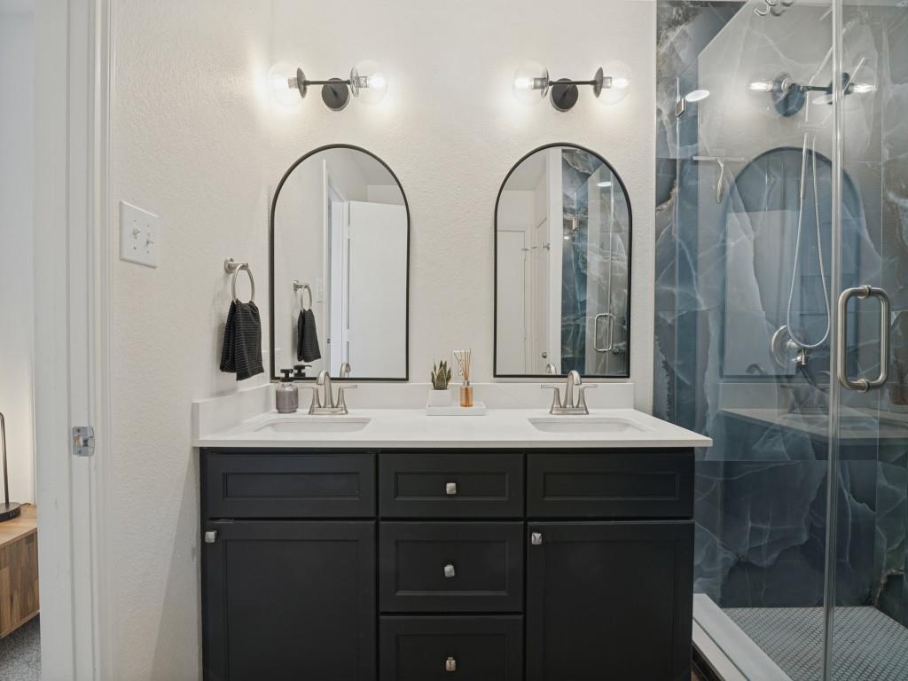 Double vanity featuring charcoal-colored cabinetry, dual undermount sinks, white solid-surface countertop, dual arched wall mirrors, and modern two-light fixtures