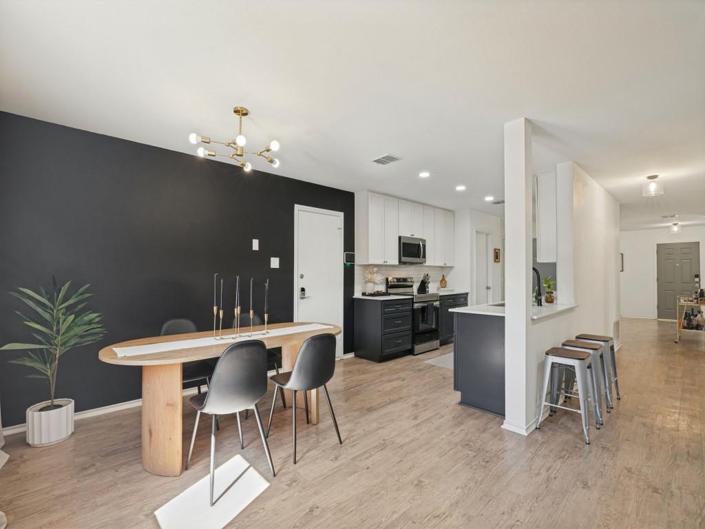 Kitchen featuring high-contrast cabinetry, stone countertops, wood-finish flooring, a breakfast bar, and a modern multi-arm chandelier