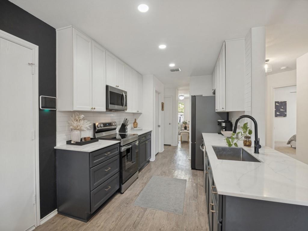 Kitchen featuring two-tone cabinetry, stone-finish countertops, subway tile backsplash, stainless steel appliances, and a matte black gooseneck faucet