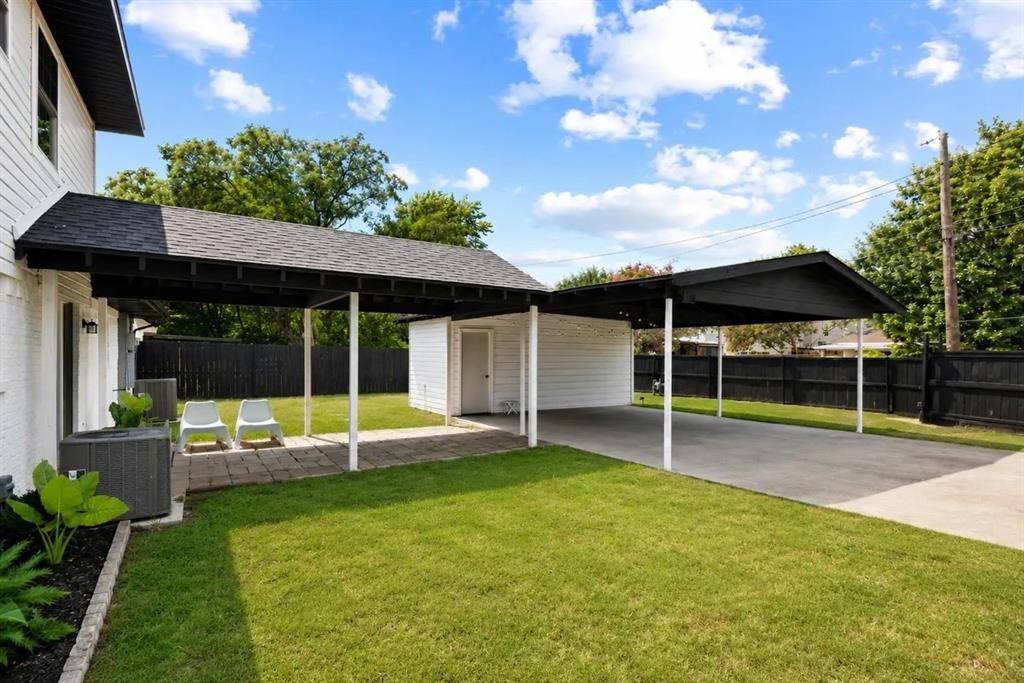 Covered carport featuring a concrete surface, shingled roof, lawn area, and perimeter privacy fencing