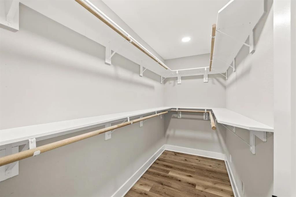 Walk-in closet featuring multi-level wooden hanging rods, white shelving, recessed lighting, and wood-finish flooring