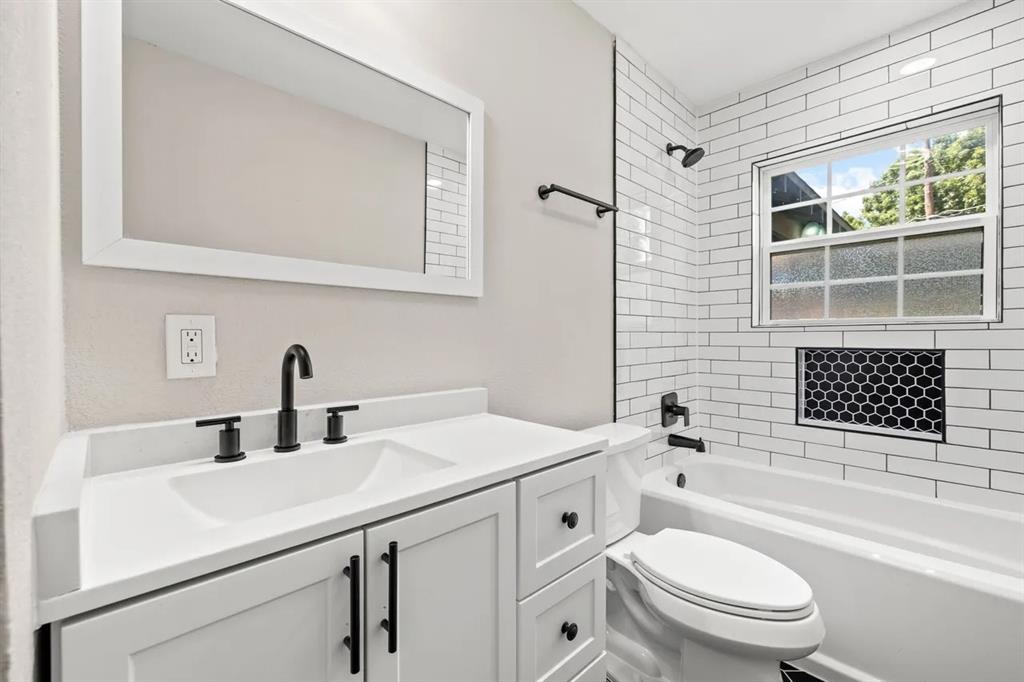 Bathroom featuring a vanity with a solid-surface countertop, subway tile shower surround with a decorative hexagonal inset, matte black fixtures, and a framed mirror