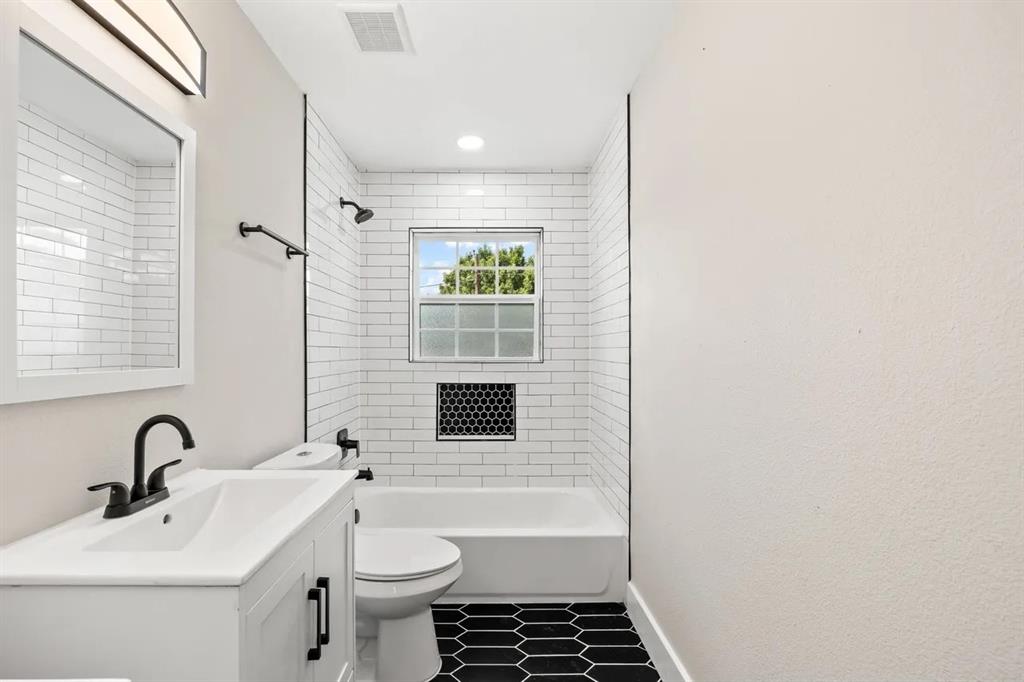 Bathroom featuring a white vanity with a rectangular sink, matte black faucet, subway-tiled tub surround with a built-in hexagonal niche, and black hexagonal floor tiling