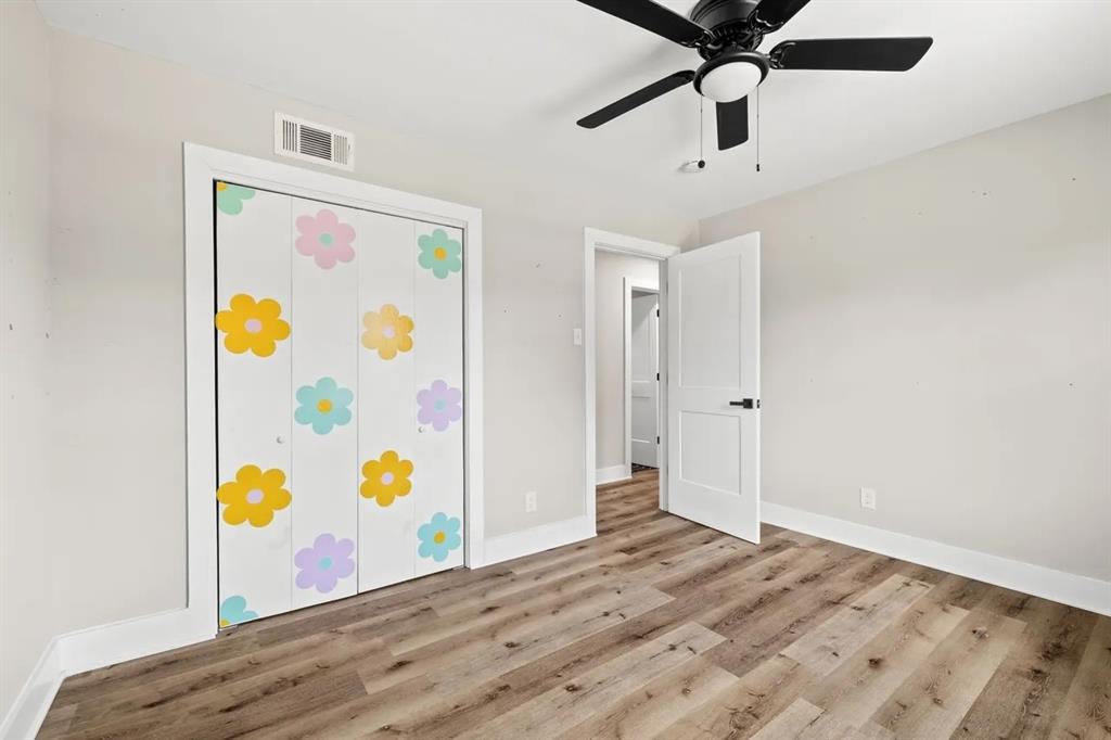 Wood-finish flooring, multi-panel interior door with matte black hardware, and a ceiling-mounted fan with integrated light fixture