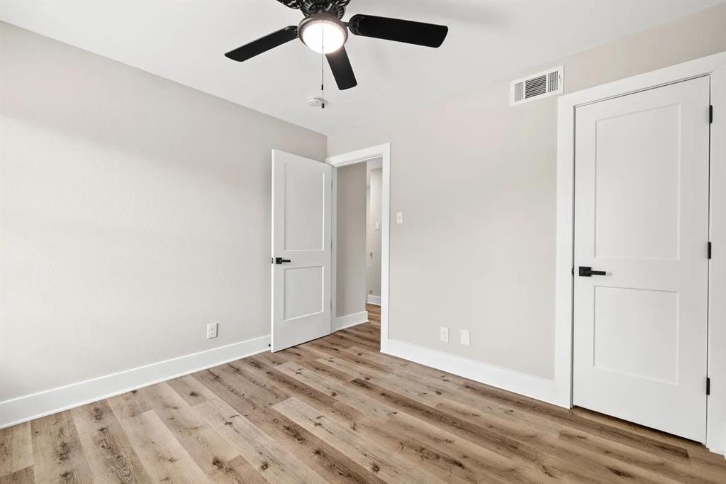 Wood-finish flooring, two-panel interior doors with matte black hardware, and a ceiling fan with integrated lighting