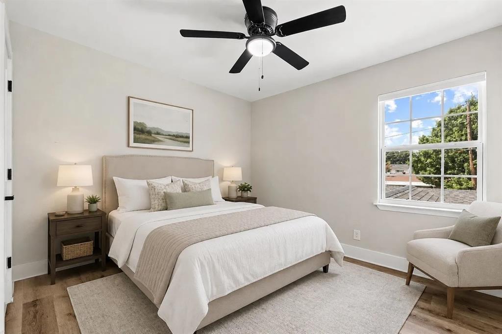 Bedroom featuring neutral wall tones, wood-finish flooring, a multi-pane window, and a central ceiling fan with an integrated light fixture