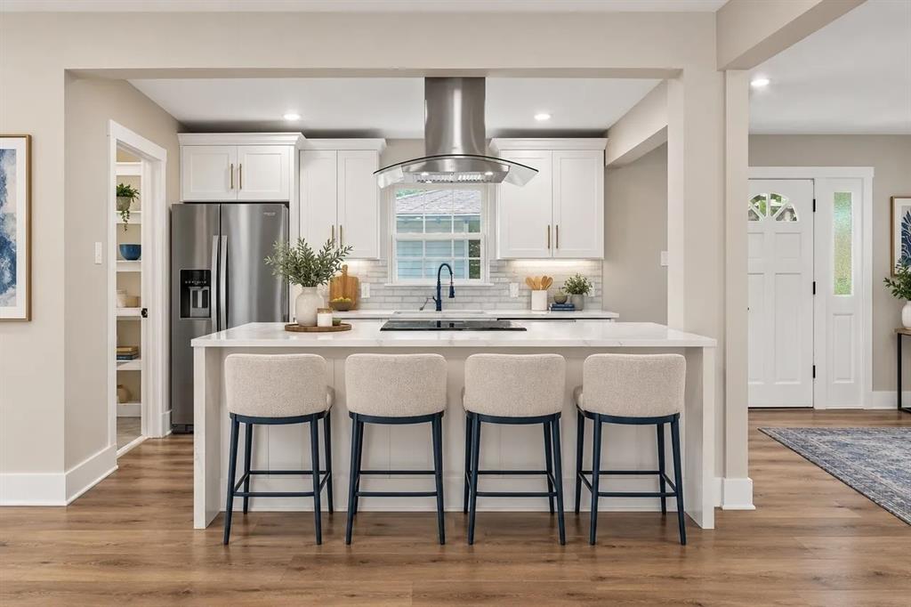 Kitchen featuring a central island with a quartz countertop, stainless steel appliances, a glass and stainless steel range hood, white cabinetry, and wood-finish flooring Kitchen featuring a central island with a quartz countertop, stainless steel appliances, a glass and stainless steel range hood, white cabinetry, and wood-finish flooring