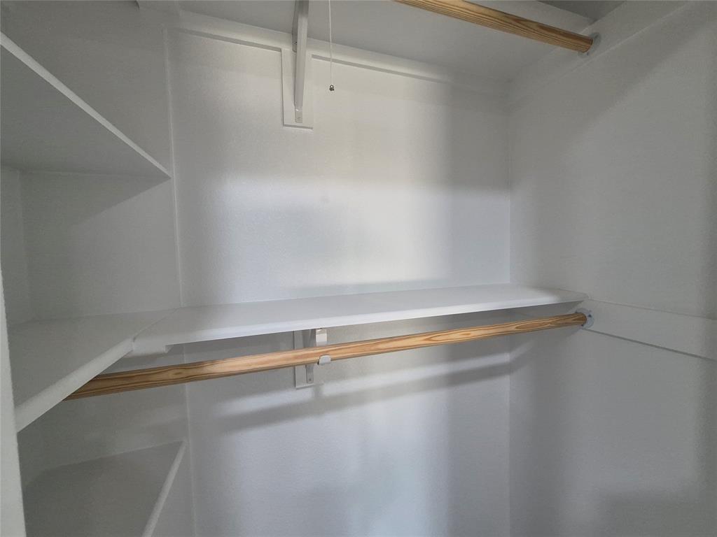 Storage closet featuring white-finished shelving and wooden clothing rods