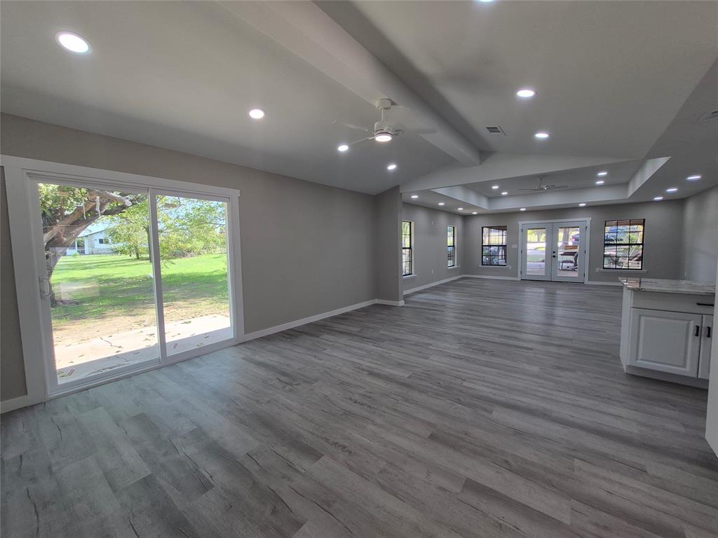 Open-concept interior featuring wood-finish flooring, recessed lighting, vaulted ceilings, a sliding glass door, and white cabinetry with stone-finish countertops