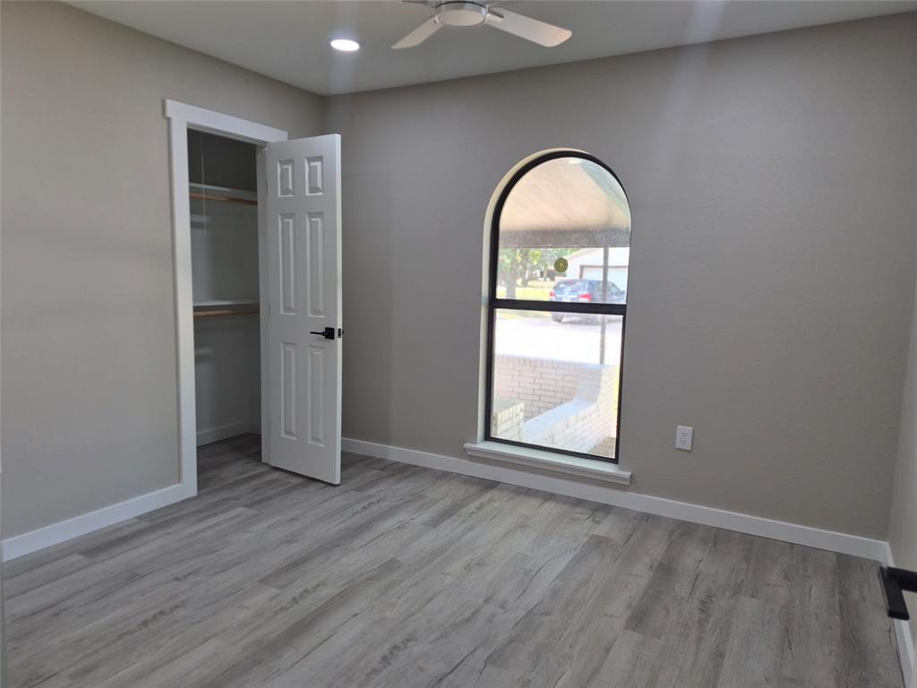 Interior space featuring wood-finish flooring, an arched window, a ceiling fan, and a walk-in closet with built-in shelving