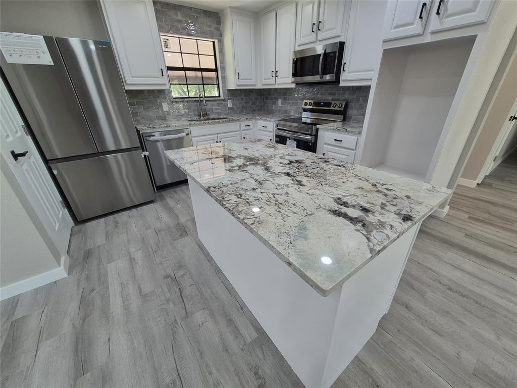 Kitchen featuring an island with stone-finish countertops, white cabinetry, stainless steel appliances, and wood-finish flooring