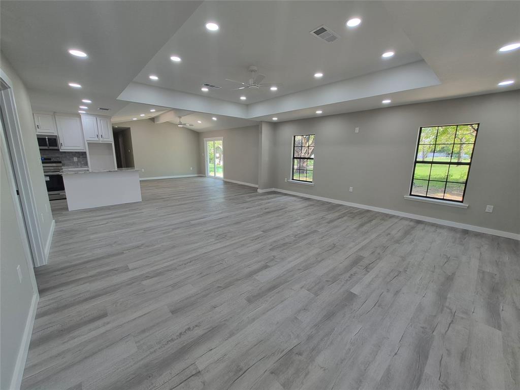 Open-concept space featuring wood-finish flooring, tray ceilings with recessed lighting, multi-pane windows, and a kitchen island with stone-surface countertop
