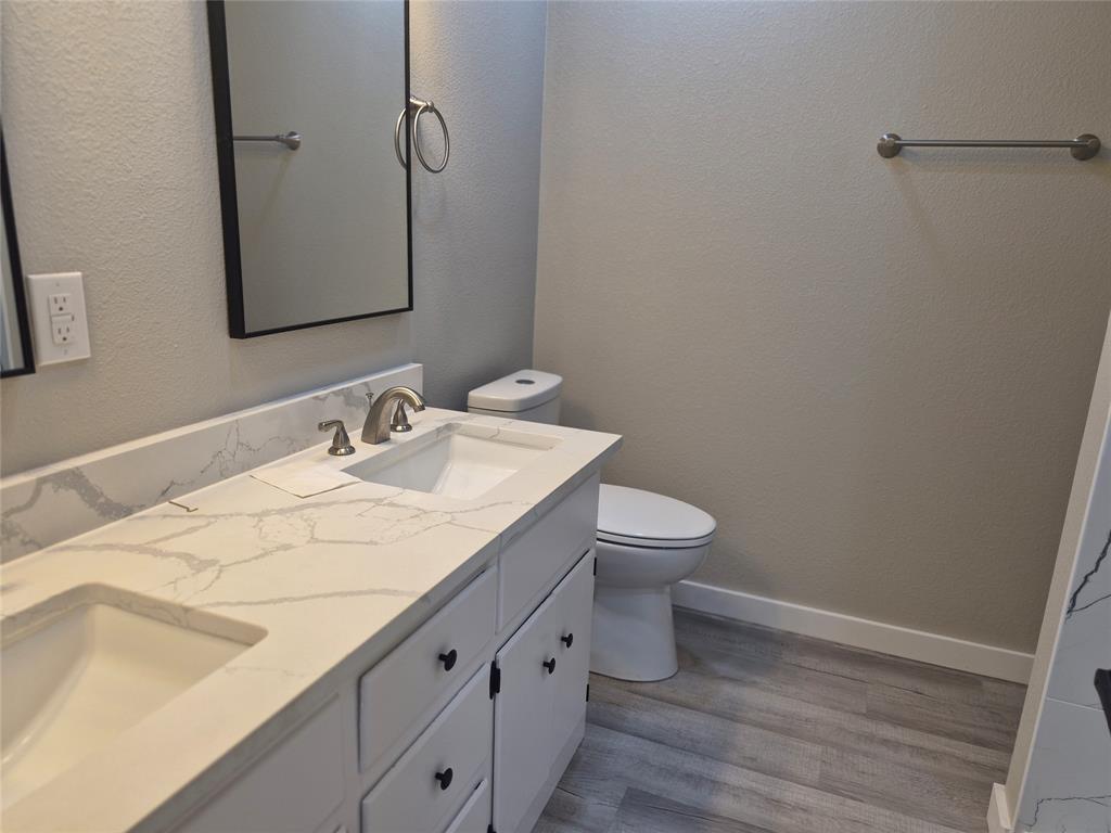 Double-sink vanity featuring stone-patterned countertops, undermount sinks, matte black hardware, and wood-finish flooring