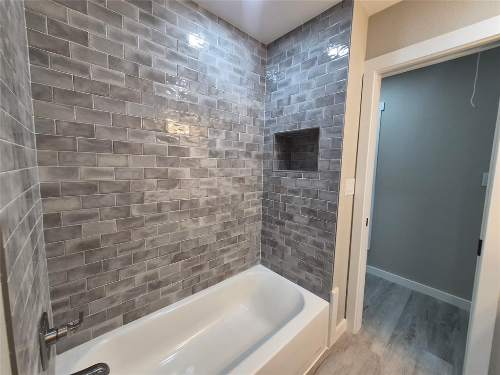 Tiled shower surround featuring glazed gray brick-style subway tiles, built-in recessed wall niche, and polished chrome hardware